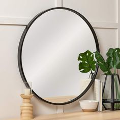 a round mirror sitting on top of a wooden table next to a plant and vase