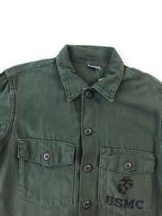 "USMC green cotton shirt circa 1971 has 'USMC' along with a globe screen printed on the chest pocket. The shirt has a button front, and cuffs, and chest pockets with buttoned flaps. Condition Overall excellent. Has some fade from wear near the back hem, a small stain near the button placket, and a tiny hole on the right arm near the shoulder. Measurements Chest 40\" Waist 38\" Shoulder 16.5\" Sleeve length 21.5\" Length 28\" Best for a size small." Classic Green Shirt With Pockets, Green Cotton Shirt With Pockets, Green Button-up Shirt With Patch Pockets, Green Cotton Shirt With Patch Pockets, Green Workwear Tops With Flap Pockets, Green Tops With Flap Pockets For Work, Green Button-up Camp Shirt With Pockets, Green Collared Camp Shirt With Button Closure, Green Unstructured Cotton Shirt