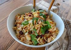 a white bowl filled with pasta and vegetables on top of a wooden table next to two chopsticks