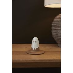 a white ghost figurine sitting on top of a wooden table next to a lamp