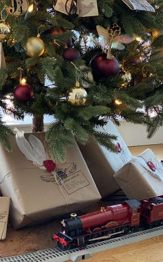 a christmas tree with presents under it and a toy train on the track next to it