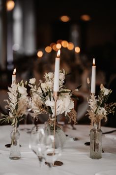 two vases with flowers are sitting on a table in front of candles and wine glasses