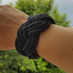 a person wearing a black rope bracelet on their arm with trees in the back ground