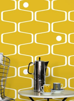 a table with a coffee pot on it next to a chair and yellow wallpaper