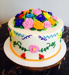 a white cake with multi colored flowers on the top and bottom, sitting on a table