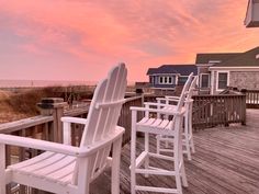 two white chairs sitting on top of a wooden deck next to the ocean at sunset