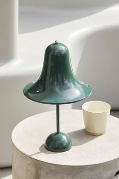 a green lamp sitting on top of a table next to a white cup and saucer