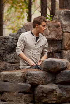 a young man standing next to a pile of rocks in the woods with his hands on his hips