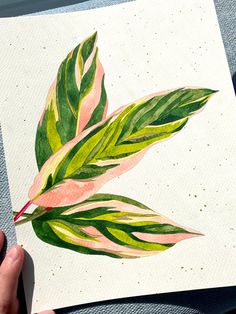 a person holding up a piece of art with green and pink leaves painted on it