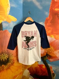 a t - shirt hanging on a wall with flowers in the background and a mural behind it