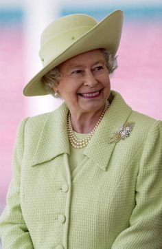 an older woman wearing a green coat and hat with pearls on it's lap