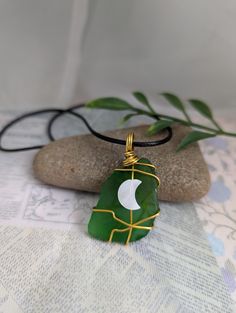 a green pendant with a white crescent on it sitting on top of a rock next to a plant