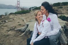 two women are sitting on the rocks by the water and one is kissing the other