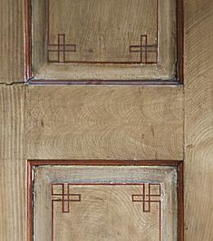 a cat is sitting on the floor in front of a wooden door with red trim