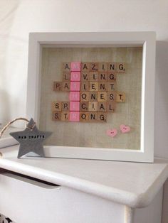 a wooden scrabble frame with pink and white tiles on it, next to a star ornament