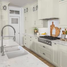 a white kitchen with marble counter tops and stainless steel faucet in the center