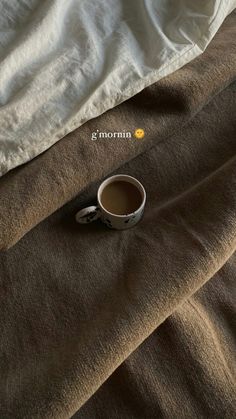 a cup of coffee sitting on top of a bed next to an unmade pillow