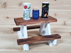 a wooden table with two cups and a bench on the top, sitting on wood planks