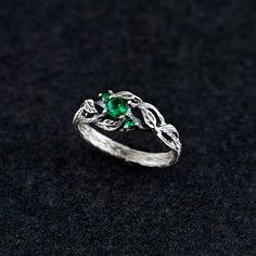 a silver ring with leaves and green stones on the side, sitting on a black surface