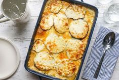 a casserole dish with meat and cheese on it next to two cups of water