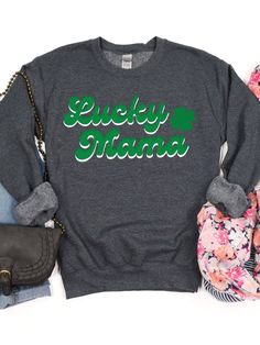 Stay warm and stylish with our Lucky Mama Women's Crewneck Sweatshirt. Featuring the words "Lucky Mama" written in a green and white retro font and a 4-leaf clover design, this sweatshirt is perfect for celebrating St. Patrick's Day or showing off your Irish heritage. Made with a high-quality Gildan Heavy Blend fabric, this sweatshirt is both durable and comfortable. Available in 3 classic colors and 6 sizes, it's perfect for any women. The crewneck design and relaxed fit make it perfect for lou Green Crew Neck T-shirt With Lettering, Green Long Sleeve Sweatshirt With Lettering, Green Long Sleeve Slogan T-shirt, Green Long Sleeve T-shirt With Slogan, Green Crew Neck Sweatshirt With Lettering, Green Letter Print Top For St. Patrick's Day, Green Long Sleeve Tops With Name Print, Green Relaxed Fit Top With Lettering, Green Top With Lettering And Relaxed Fit