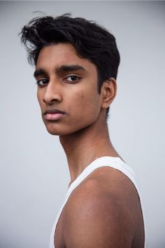 a young man with black hair and no shirt is looking at the camera while wearing a white tank top