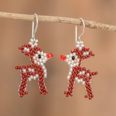 two red and white beaded reindeer earrings hanging from a branch