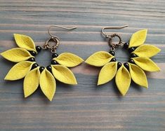 two pairs of earrings with yellow leaves and black beads on wooden background, closeup