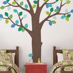 two beds in a room with a tree painted on the wall