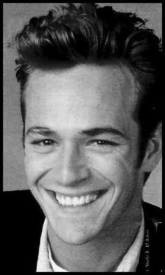 a black and white photo of a man smiling for the camera with his hair pulled back