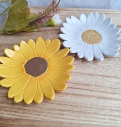 two yellow and white flowers sitting on top of a wooden table next to each other