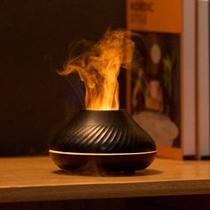 a fire burning inside of a black vase on top of a wooden table next to a bookshelf