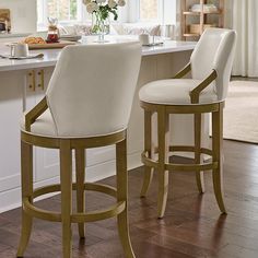 two white bar stools sitting in front of a kitchen island with flowers on it