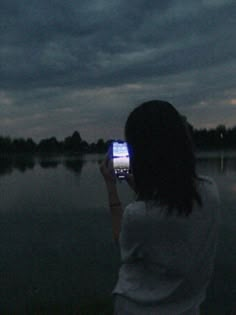 a woman is taking a photo with her cell phone at night by the water's edge