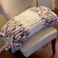 a stack of blankets sitting on top of a white chair next to a wooden floor