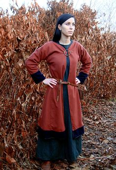 a woman standing in front of a bush wearing a red and black dress with long sleeves