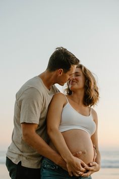 a pregnant couple embracing each other on the beach