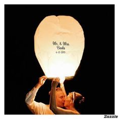 a man and woman holding up a paper lantern in the shape of a kissing couple