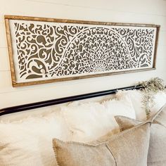 a white bed topped with pillows next to a wooden framed wall hanging over it's headboard