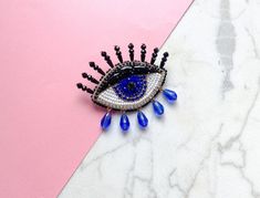 an evil eye brooch on a pink and white marble surface with blue tears