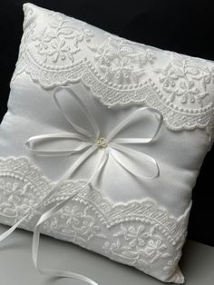 a white ring pillow with a ribbon on the side and lace trim around the edge