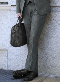 a man in a suit and tie holding a brown bag while standing against a wall