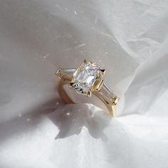 an engagement ring with three baguettes on it sitting on a white fabric background