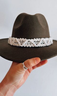 a woman's hand holding a brown hat with white crochet on it