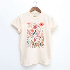 Looking for a cute versatile top to wear this summer? Make sure to grab one of our Pastel Wildflowers garment dyed graphic tees! This soft and comfortable graphic tee is the perfect top for any outfit. It can be paired with biker shorts, jeans, or even a simple skirt/dress! This tee is true-to-size, so be sure to order your regular t-shirt size! If you are looking for a more oversized look, make sure to size up! Beige Graphic Tee For Summer, Beige Screen Print T-shirt For Summer, Summer Beige T-shirt With Screen Print, Casual Watercolor Print T-shirt With Relaxed Fit, Summer Cotton Floral Print T-shirt, Relaxed Fit Organic Cotton T-shirt For Summer, Beige Cotton T-shirt For Summer, Cute Spring Tops In Organic Cotton, Vintage Cotton T-shirt With Plant Print