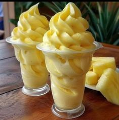 three cups filled with ice cream sitting on top of a wooden table next to slices of pineapple