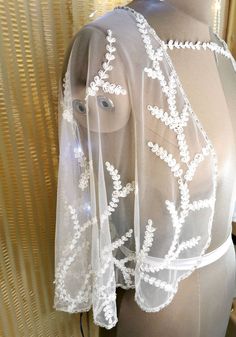 a mannequin wearing a sheer white cape with flowers on it