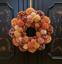 an orange and brown wreath hanging on a black door with gold trimmings in front of it