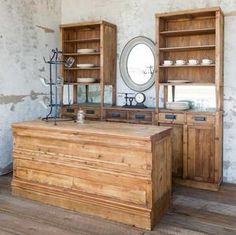 an old fashioned kitchen with wooden cabinets and dishes on the counter top in front of a round mirror