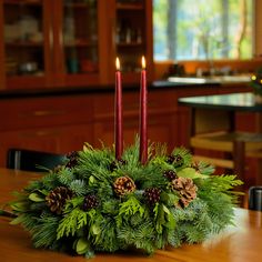 a christmas centerpiece with pine cones, holly and red candles on a dining room table